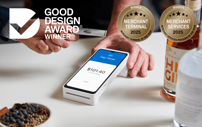 A person taps a card on a payment terminal displaying $101.40. Two award badges and a bottle of gin are visible on the table.